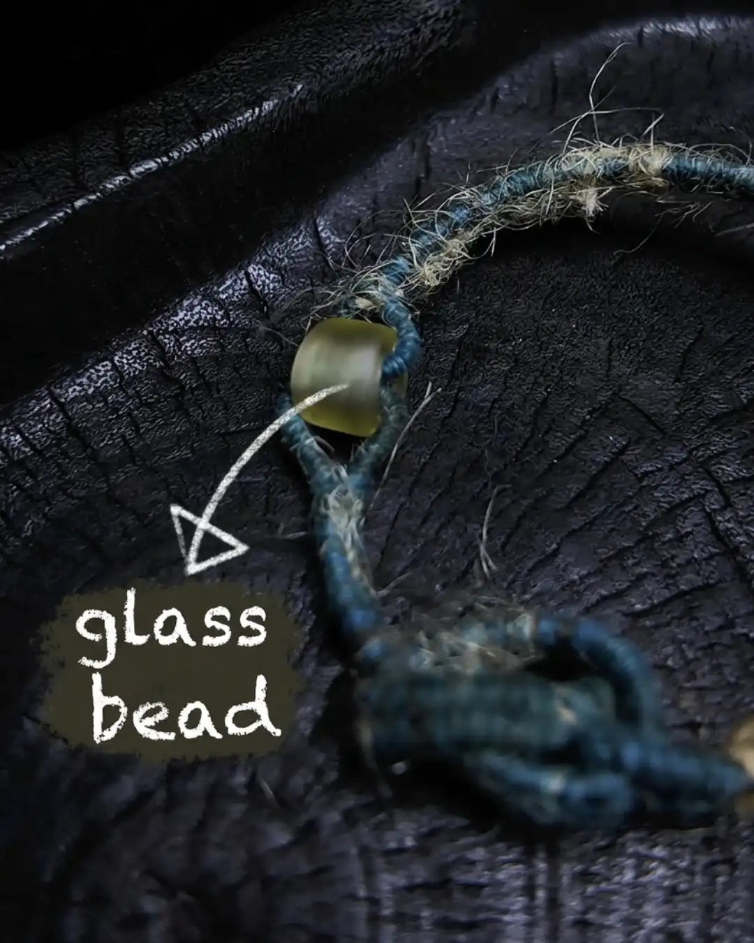 Glass bead detail from The Zen #08 — labelled glass bead at the adjustable knot end of the hand-knotted energy bracelet on plant-dyed cotton thread.