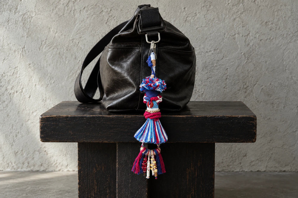 Red, blue and white textile bag charm hanging from a black leather bag on a dark wooden bench