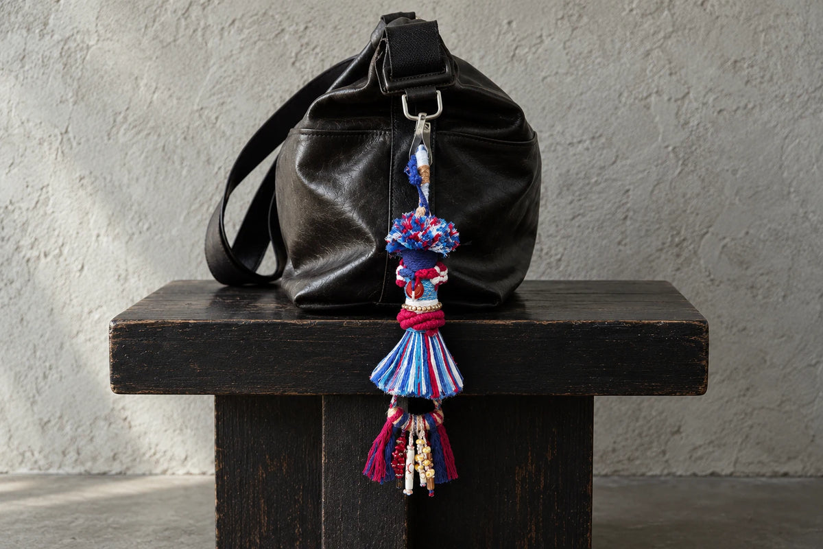 Red, blue and white textile bag charm hanging from a black leather bag on a dark wooden bench