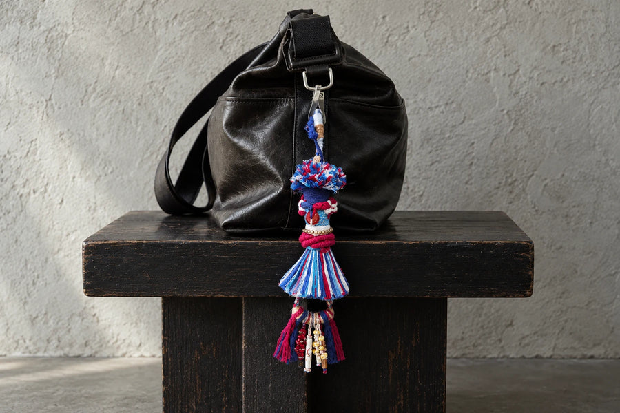 Red, blue and white textile bag charm hanging from a black leather bag on a dark wooden bench