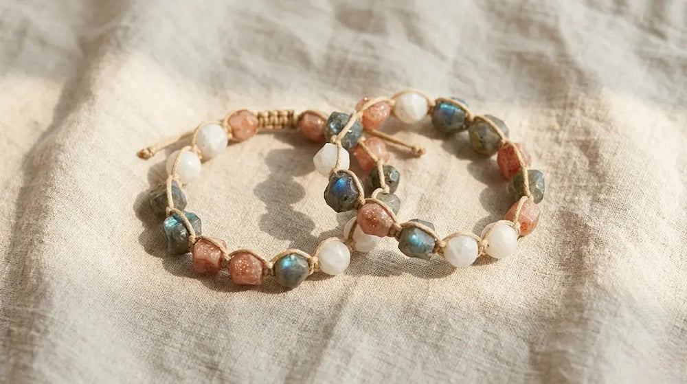 Two paired à la luck hand-knotted talismans laid on raw linen — same stone lot, knotted on the same evening, sent into two separate lives. Real natural stone, plant-dyed cotton cord, no metal.
