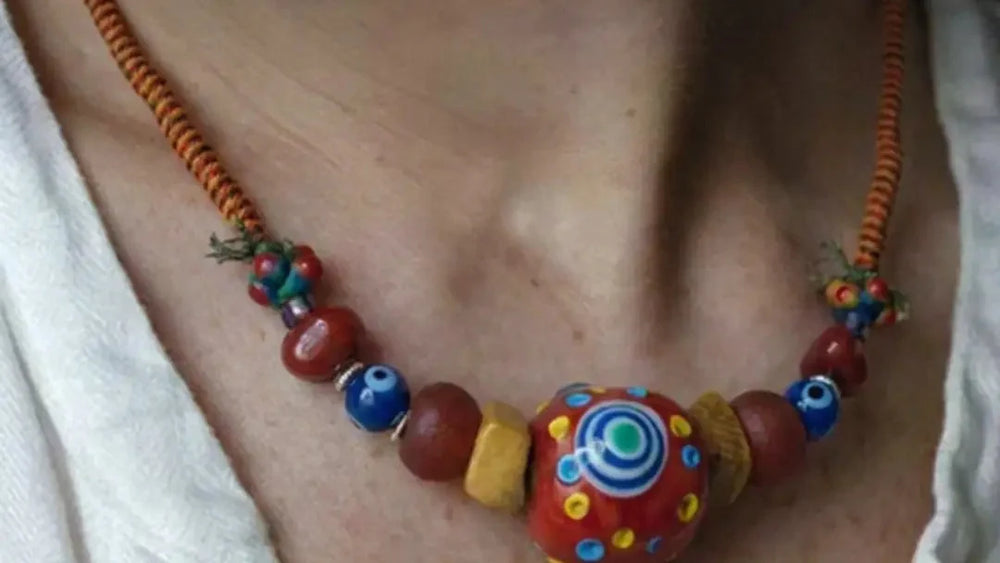 The Aegis #30 worn at the collarbone with a 33 mm Nepali estate dragonfly-eye bead, red Agate, glass eye beads, yak bone, and wrapped cord