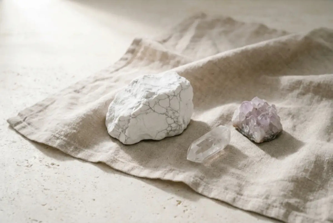 Three natural clarity crystals on oatmeal linen â a white magnesite chunk with grey veining, a clear quartz point, and a pale amethyst cluster â placed with calm negative space, illustrating a guide to crystals for mental clarity and focus.