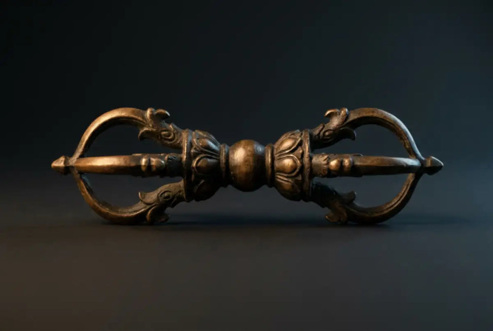 Antique five-pronged Tibetan Buddhist vajra (dorje) ritual scepter in aged bronze, perfectly symmetrical, prongs curving inward to a closed point on a dark slate ground — the adamantine emblem of the Vajrayana path.