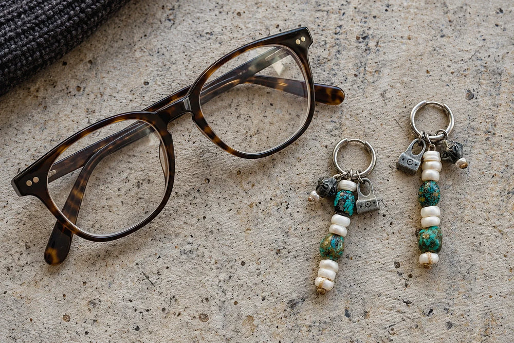 Tortoiseshell glasses beside Turquoise and Pearl drop earrings on a stone surface