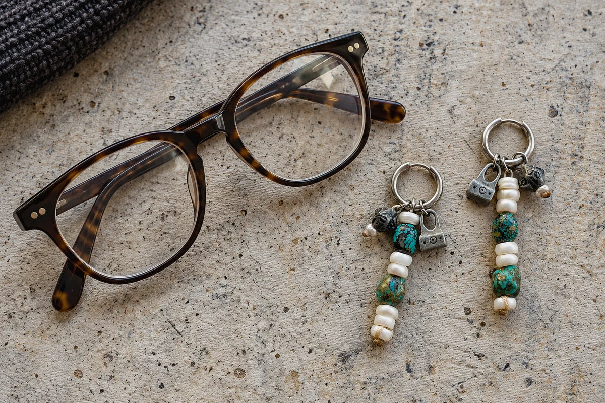 Tortoiseshell glasses beside Turquoise and Pearl drop earrings on a stone surface