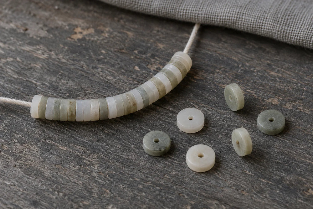Illustration of pale disc-shaped beads on cord, with loose discs showing their central holes and edge profiles.