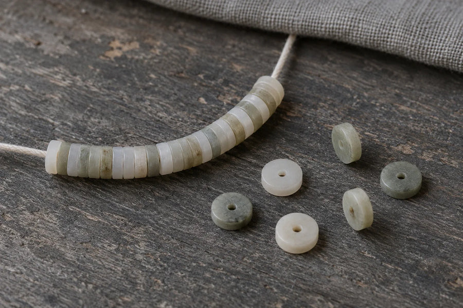 Illustration of pale disc-shaped beads on cord, with loose discs showing their central holes and edge profiles.