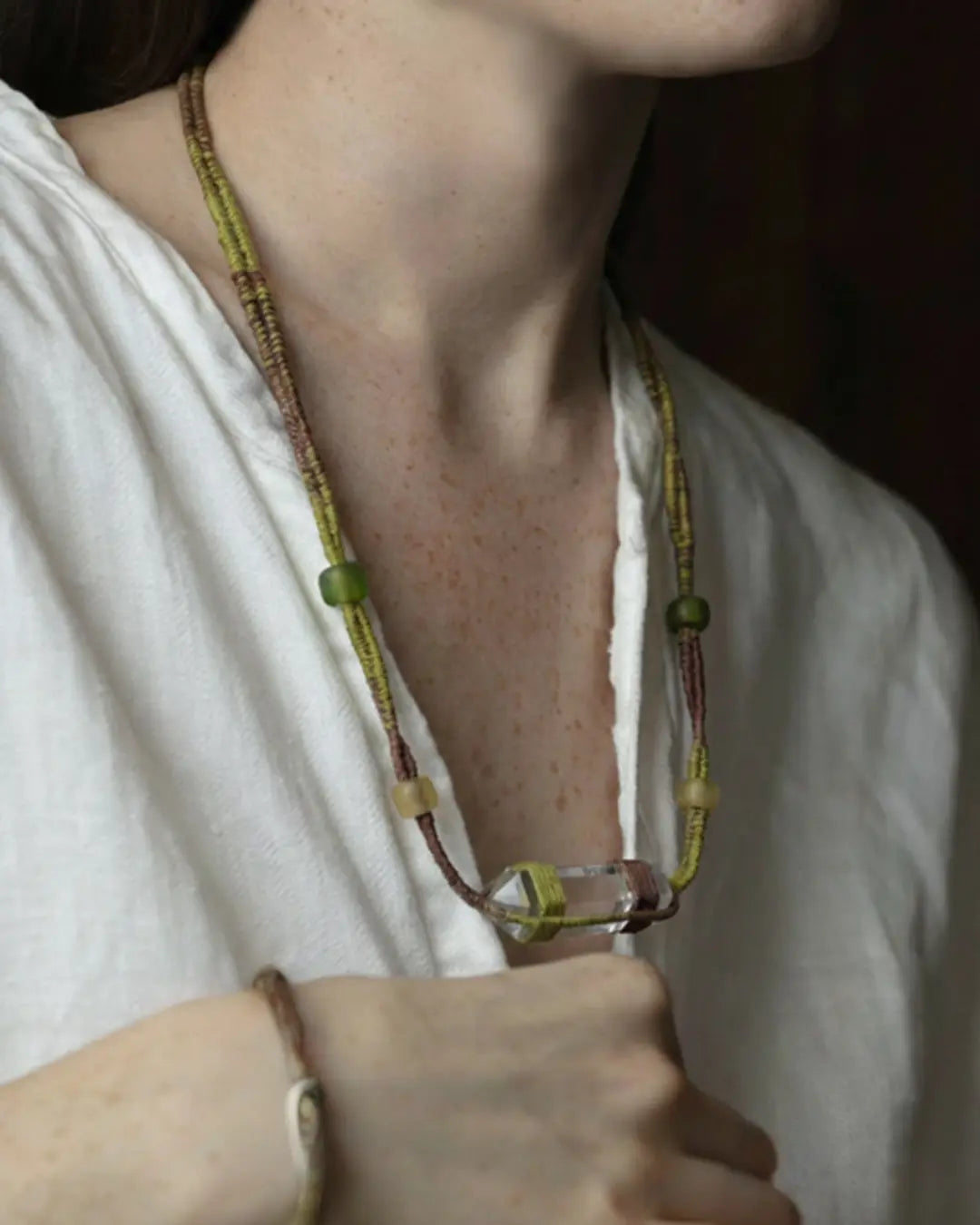 The Mindfulness #01 Himalayan clear quartz wrap bracelet and necklace by à la luck — worn at the neckline showing the raw quartz centerpiece in green silk and plant-dyed cotton thread, with the matching bracelet on the wrist.