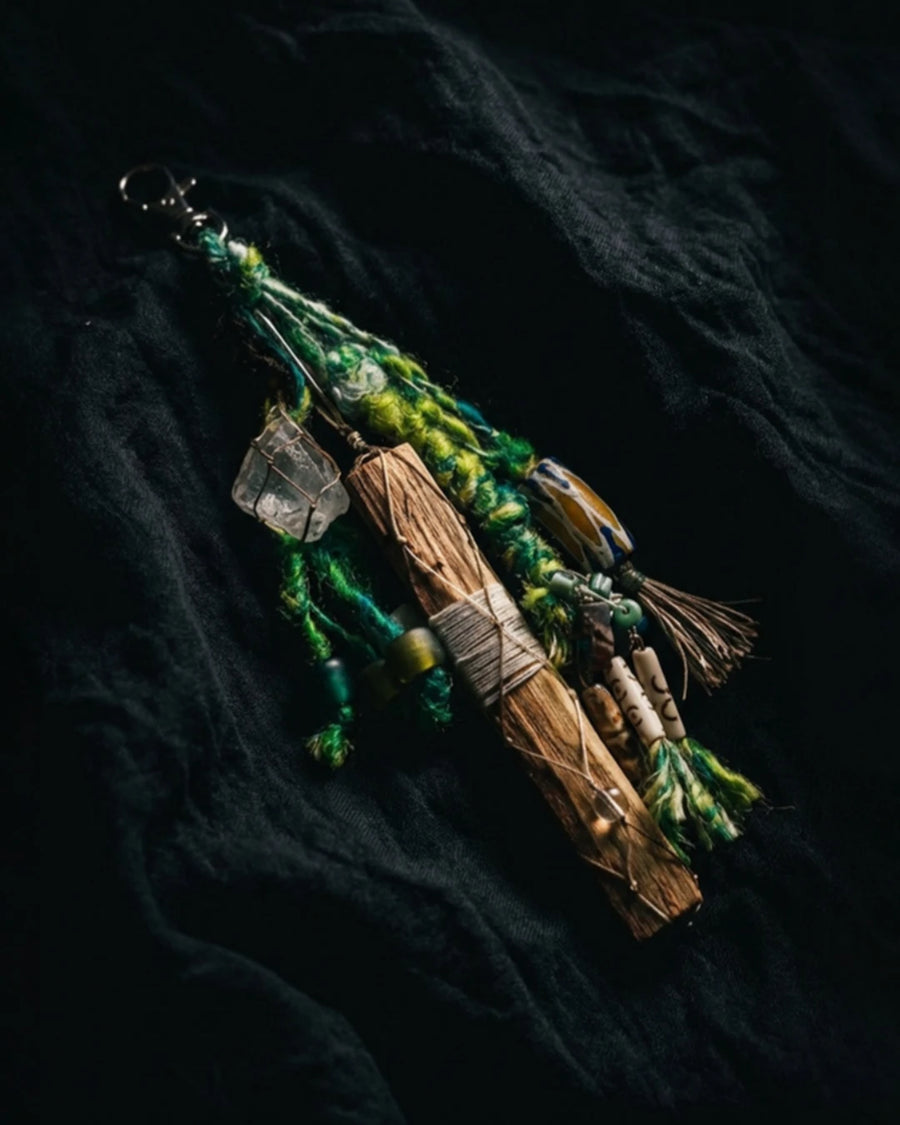 The Sanctuary #02 palo santo and quartz bag talisman by à la luck — full edition-of-one piece on dark linen showing the wrapped palo santo stick, wire-wrapped clear quartz, African trade bead, and Nepali silk yarn tassel.