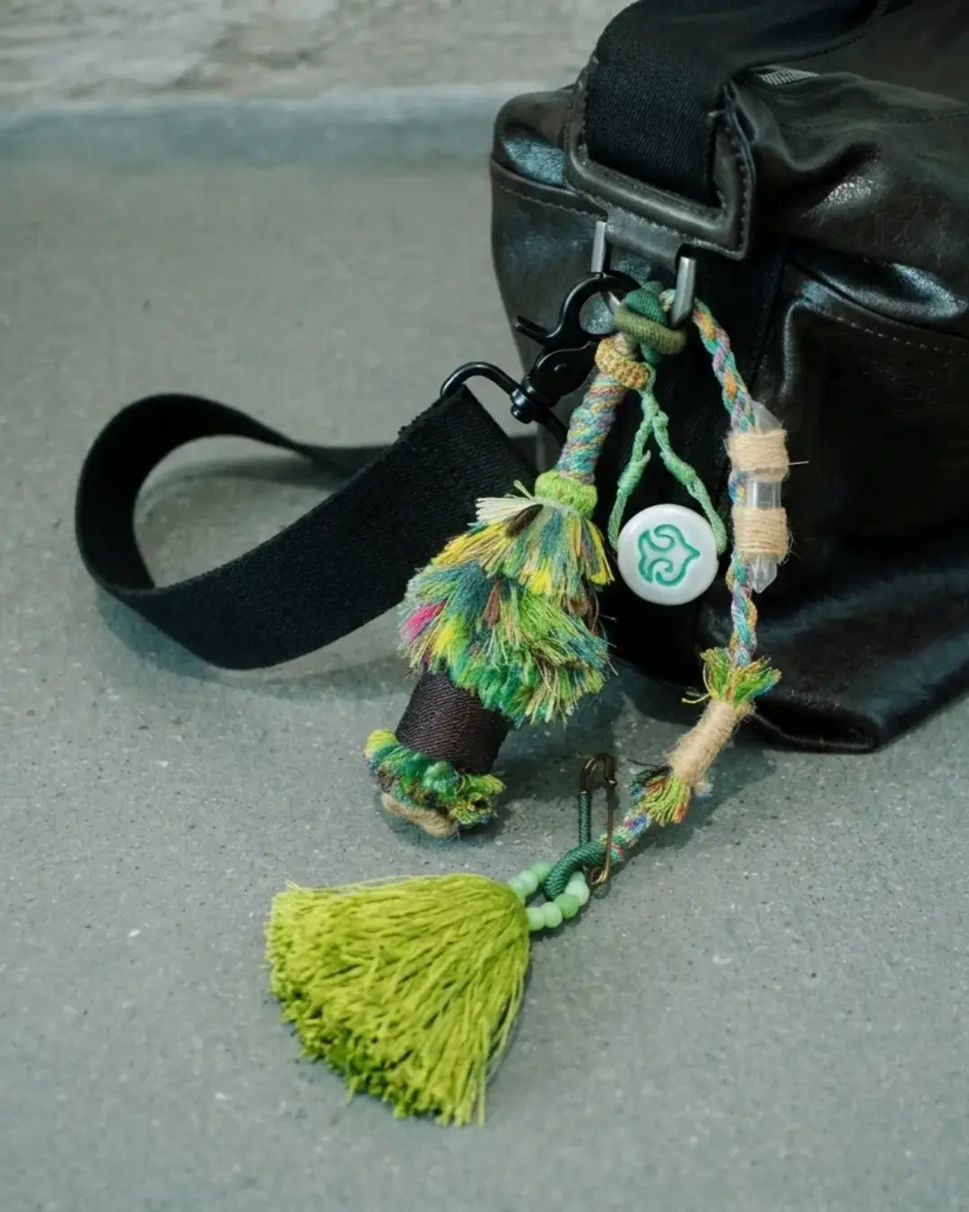 The Tree of Life #04 manifest abundance bag tassel by à la luck — full edition-of-one piece hanging from a black bag strap showing the hand spun cotton tassel tree, ceramic bead, and glass beads with brass pin.