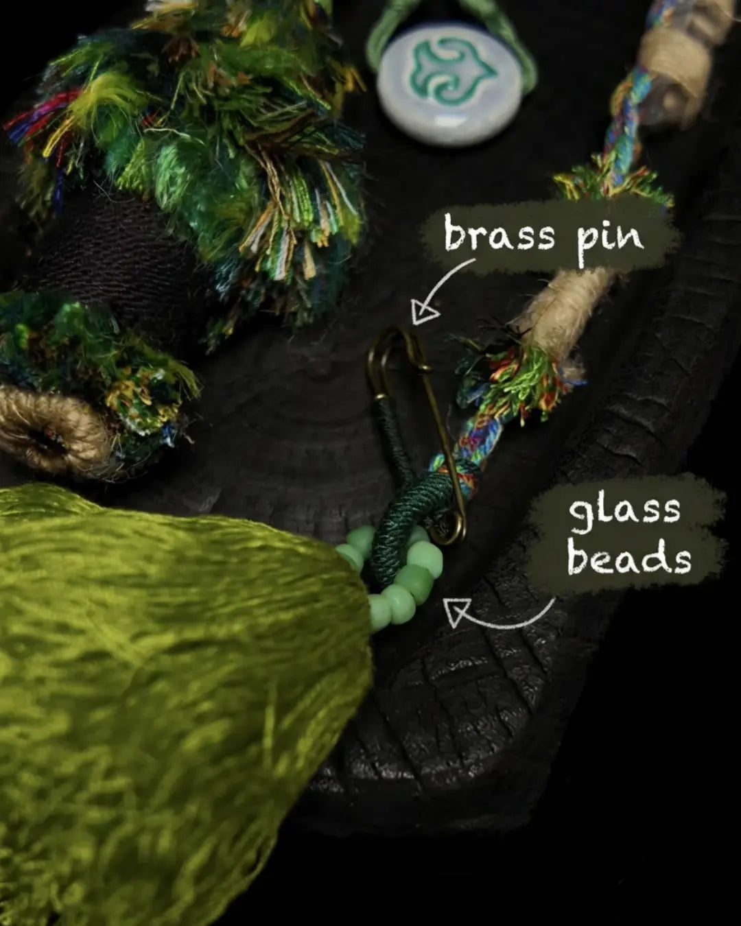 Material detail for The Tree of Life #04 — labelled brass pin and glass beads at the attachment point of the hand-knotted bag talisman.