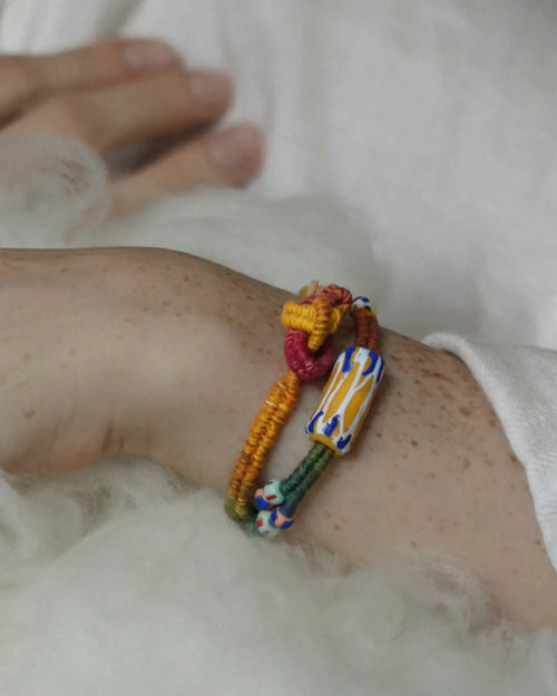 The Nomad #05 African trade bead wrap bracelet and choker by à la luck — worn on the wrist showing the bold African trade bead focal in yellow, white, and blue on multicolor plant-dyed cotton thread.