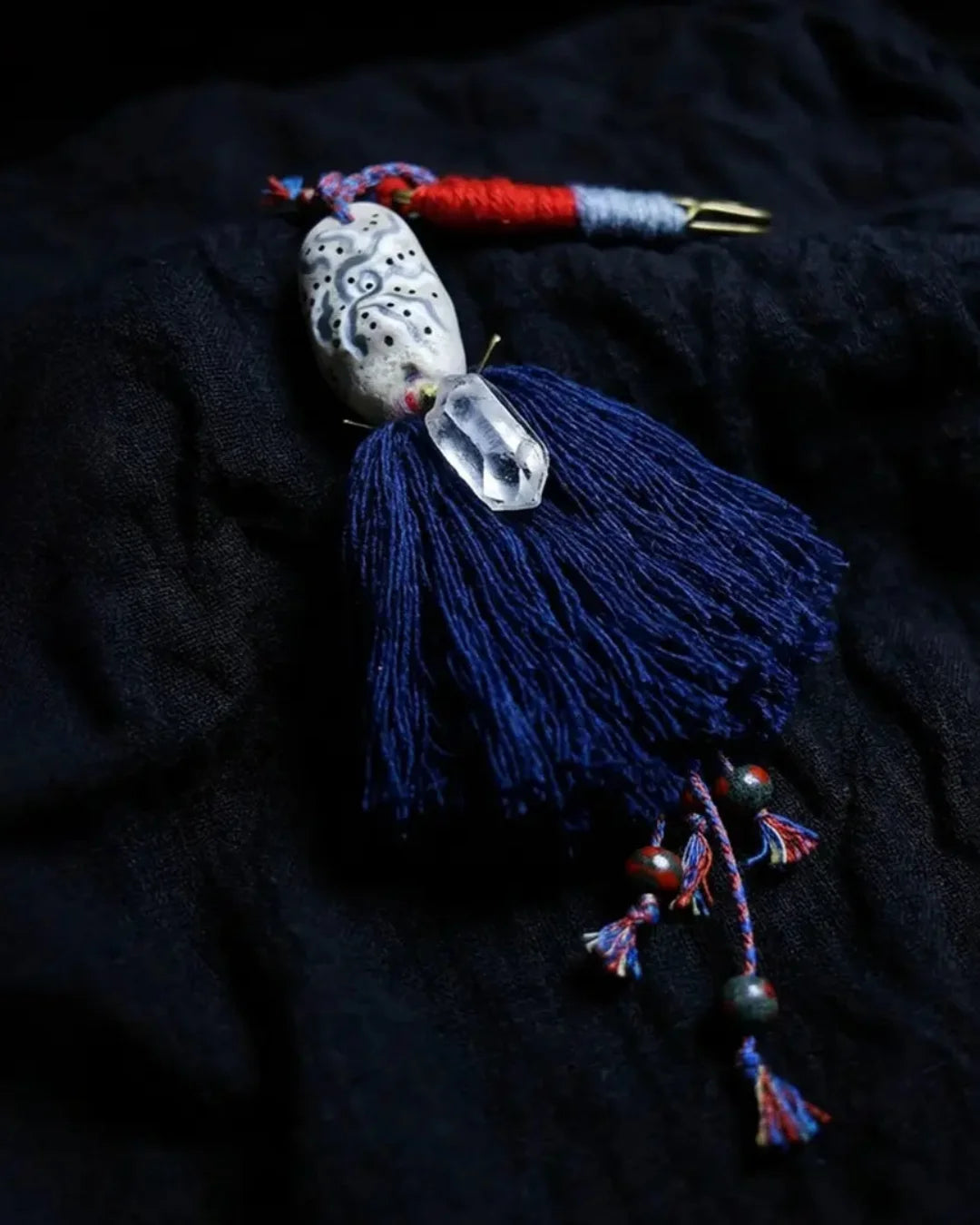 The Oracle #06 hand-painted clay and quartz bag talisman by à la luck — full edition-of-one piece on dark linen showing the hand-painted stone clay bead face, hand spun cotton tassel, and Himalayan clear quartz drop.