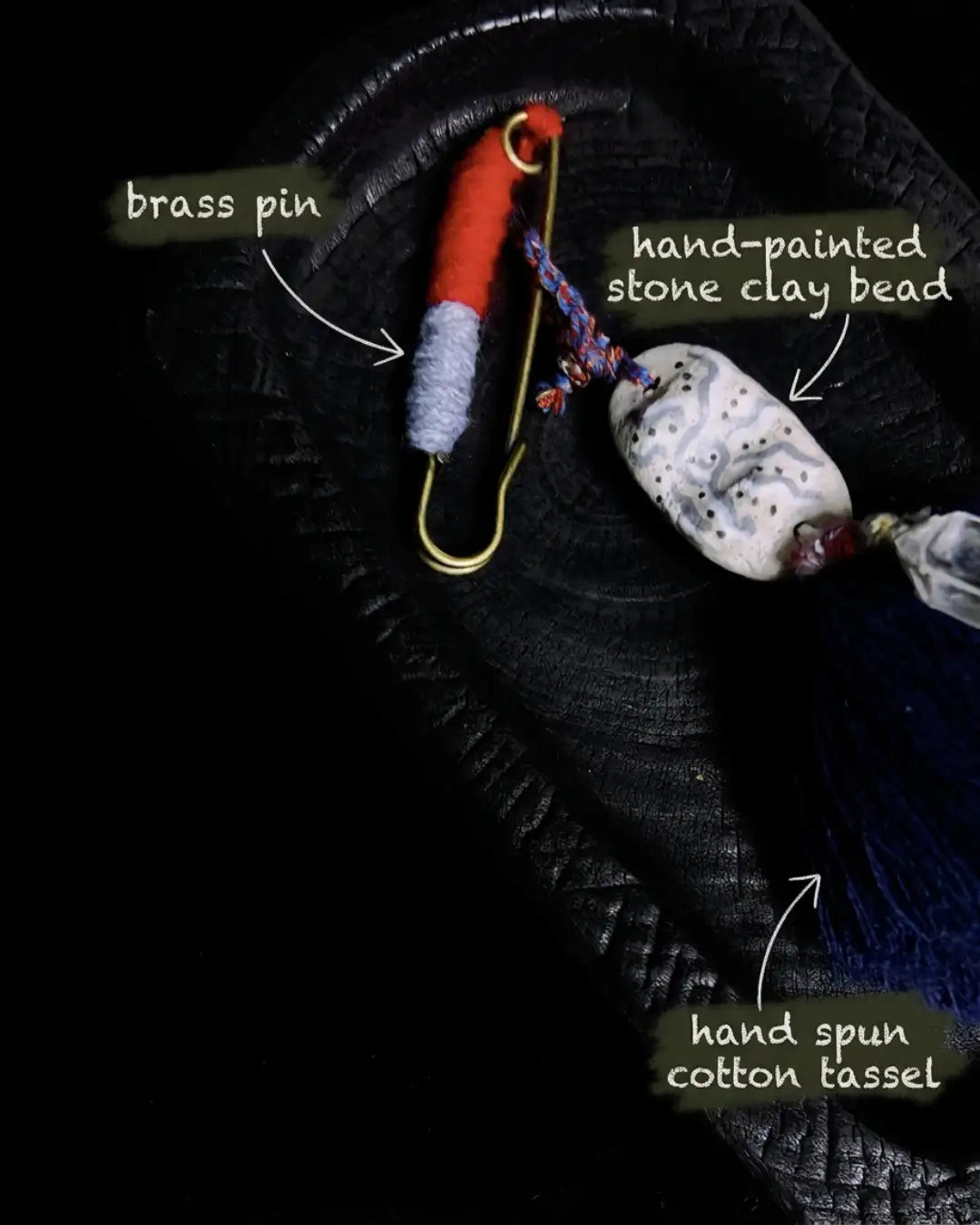 Material map for The Oracle #06 — labelled brass pin, hand-painted stone clay bead, and hand spun cotton tassel forming the upper section of the bag talisman.