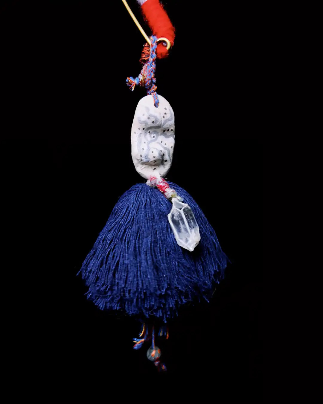 The Oracle #06 hand-painted clay and quartz bag talisman by à la luck — suspended on black background showing the full piece with hand-painted stone clay bead, navy hand spun cotton tassel, and brass pin.