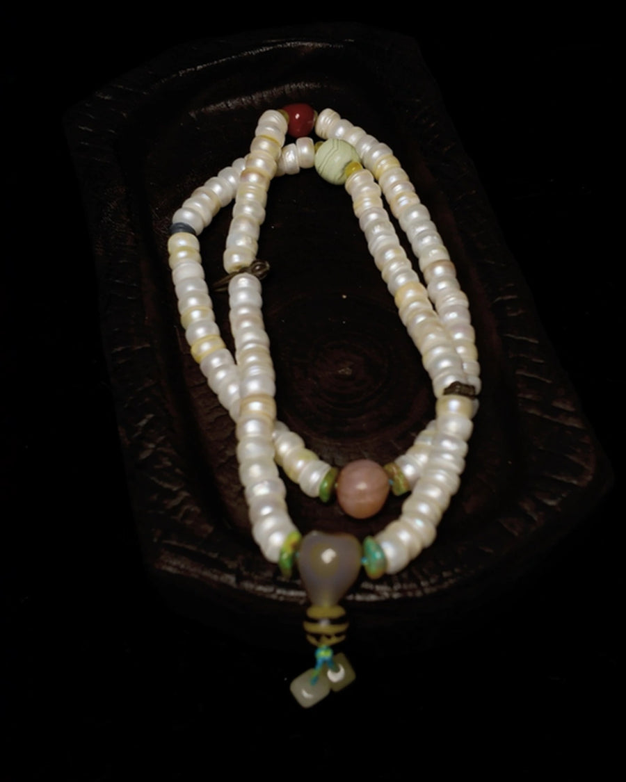 The Devotion #07 8mm pearl heishi 108 mala by à la luck — full piece on carved wood tray showing fresh water pearl heishi beads, gray lace agate focal, yak bone bead, and Hetian white jade tassel drops.