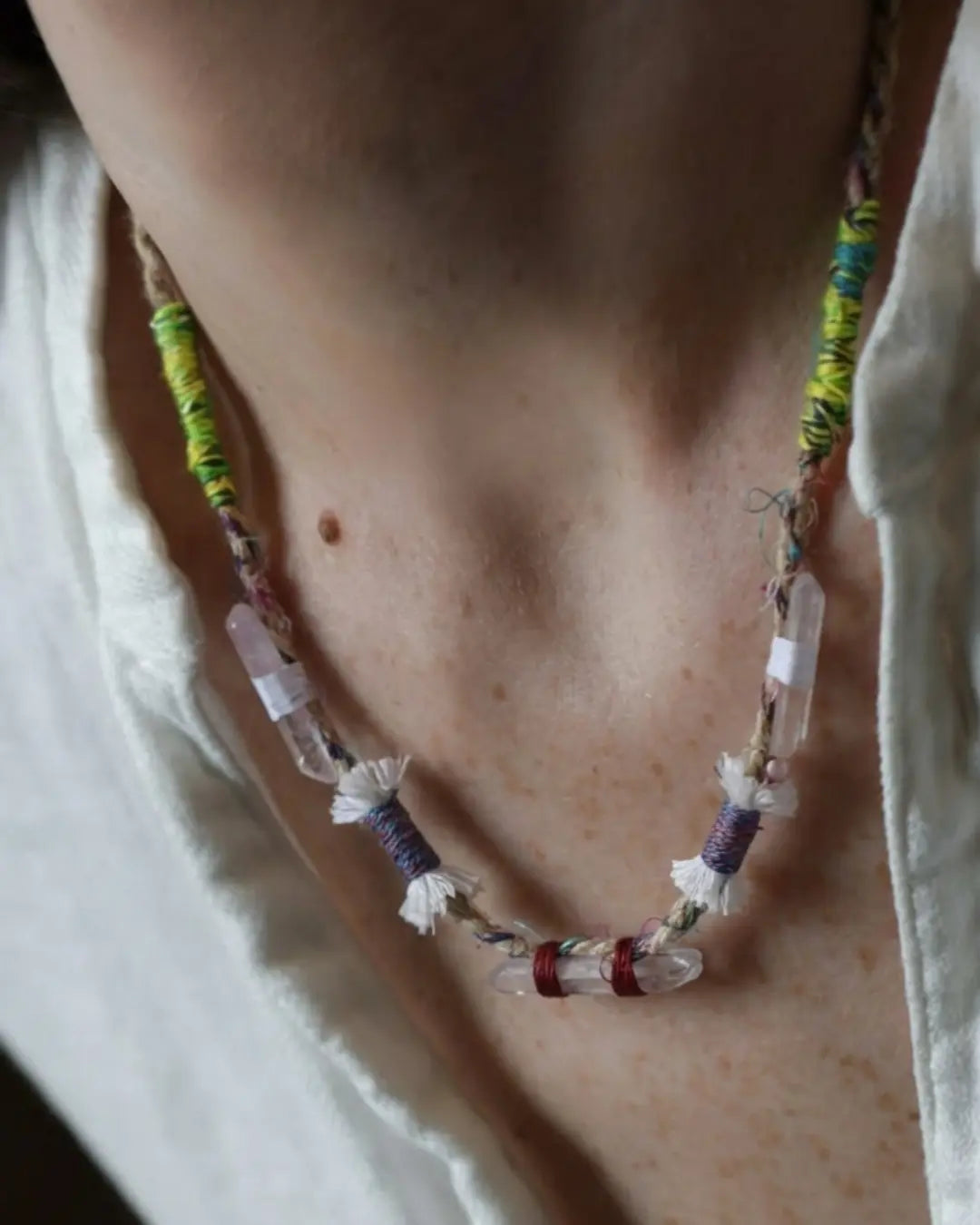The Primal #11 Himalayan clear quartz multi-point necklace by à la luck — worn at the neckline on a white shirt showing five quartz points wrapped in Nepali banana silk yarn and hand spun cotton tassel knots.