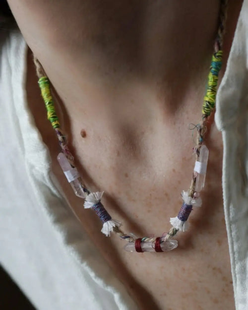 The Primal #11 Himalayan clear quartz multi-point necklace by à la luck — worn at the neckline on a white shirt showing five quartz points wrapped in Nepali banana silk yarn and hand spun cotton tassel knots.