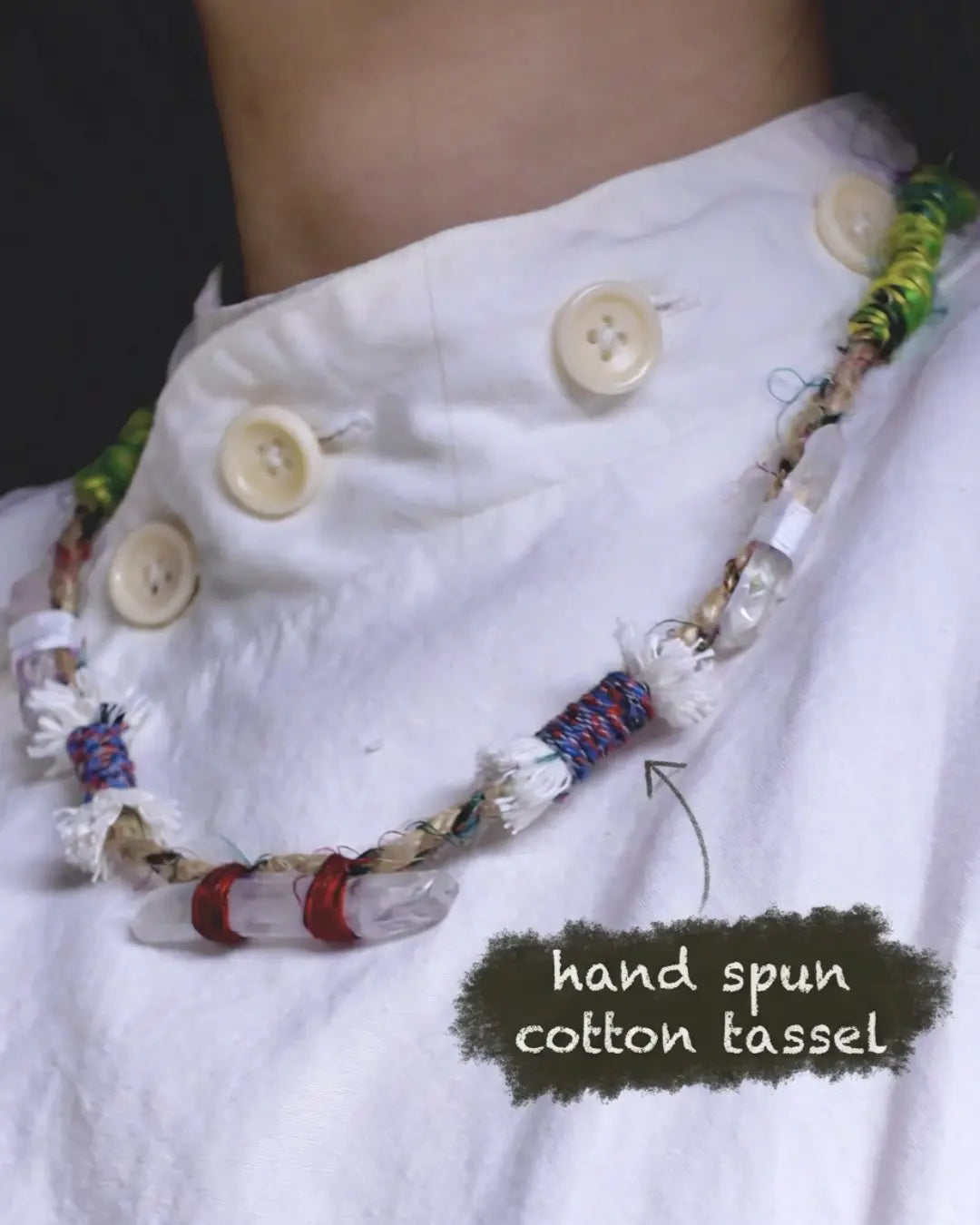 Detail of The Primal #11 worn at the neckline — labelled hand spun cotton tassel knot detail around a Himalayan clear quartz point on multicolor Nepali banana silk yarn.