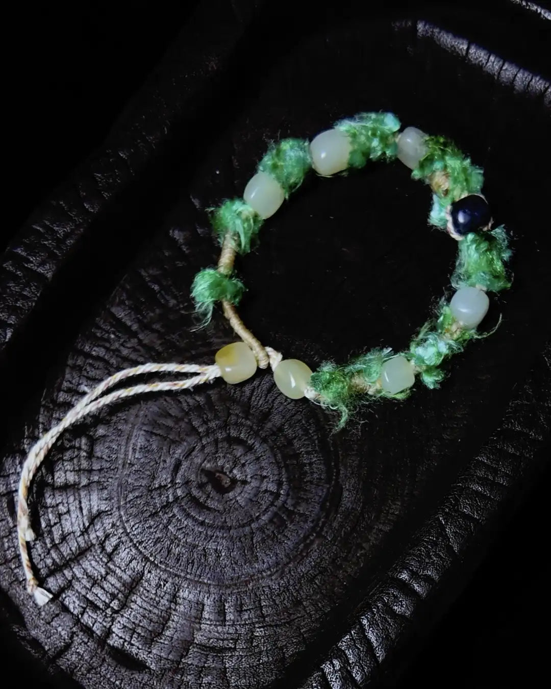 The Oasis #13 hetian jade bracelet by à la luck — full edition-of-one piece flat in charred wood bowl showing hetian white jade and hetian green jade beads on green Nepali banana silk yarn.
