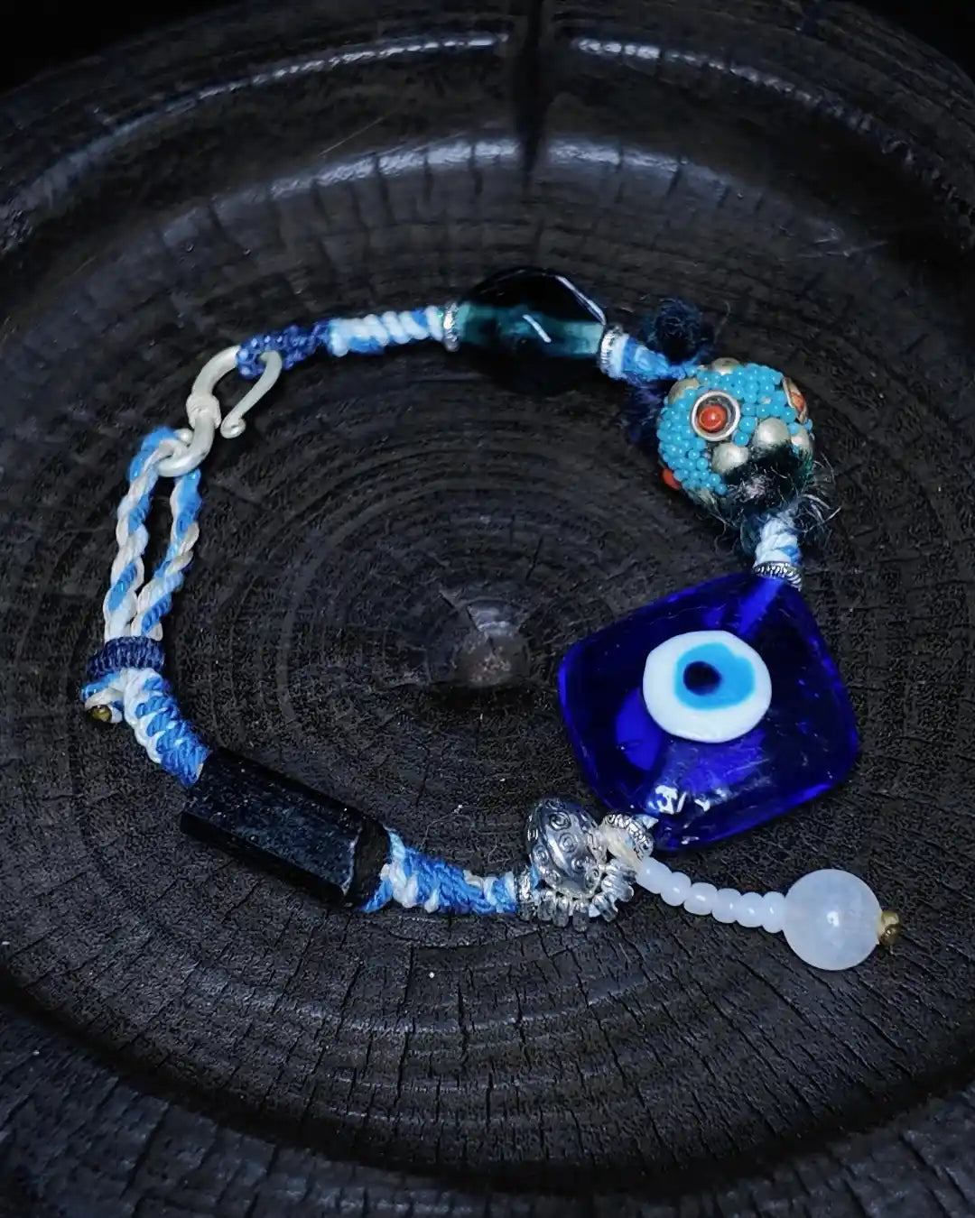 The Sentinel #15 evil eye and black tourmaline talisman bracelet shown flat on charred wood — full edition-of-one bracelet by à la luck