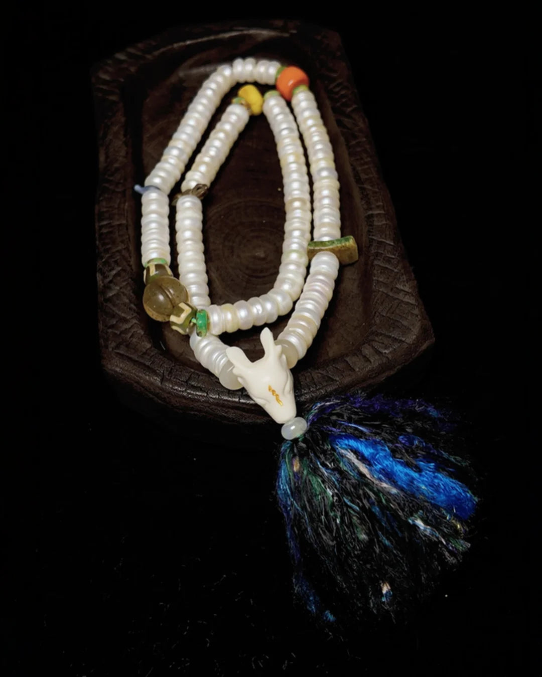 Hand-knotted pearl mala necklace with gemstone beads, tassel, and animal head pendant on wood tray
