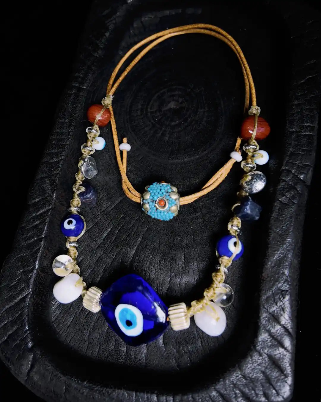 The Seer #19 evil eye and raw sapphire protection necklace shown flat on charred wood — full edition-of-one necklace by à la luck with adjustable closure visible