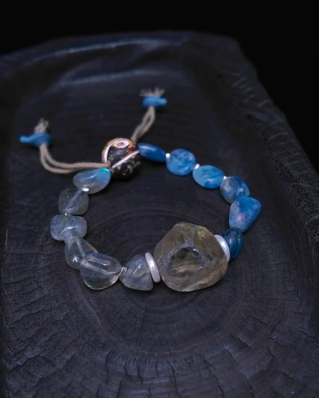 The Witness #24 smoky quartz and labradorite bracelet, full flat lay on dark wood surface showing complete bead arrangement