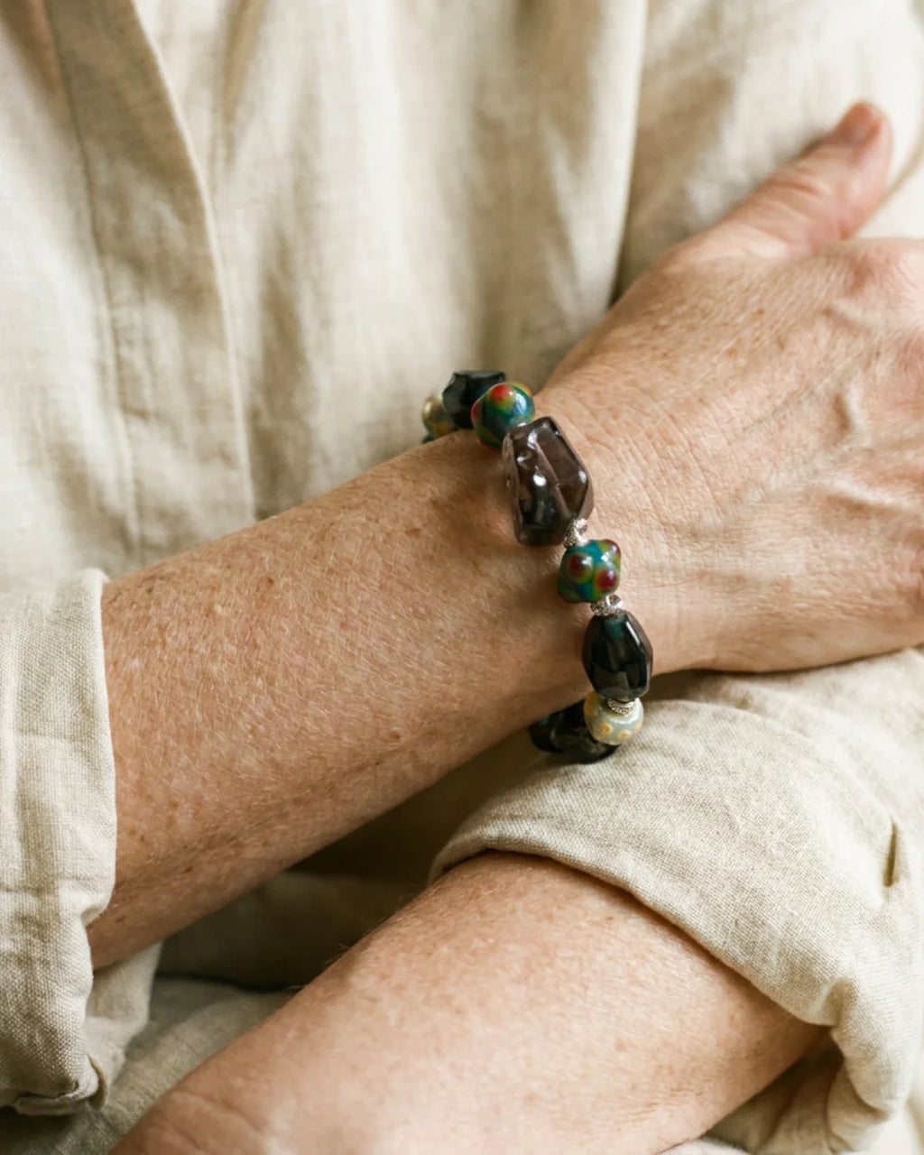 The Warden #32 smoky quartz and Tibetan dzi protection bracelet worn on wrist, lifestyle shot showing smoky quartz focal and colorful dragonfly eye glass beads