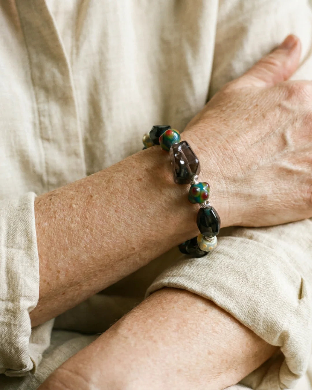 The Warden #32 smoky quartz and Tibetan dzi protection bracelet worn on wrist, lifestyle shot showing smoky quartz focal and colorful dragonfly eye glass beads
