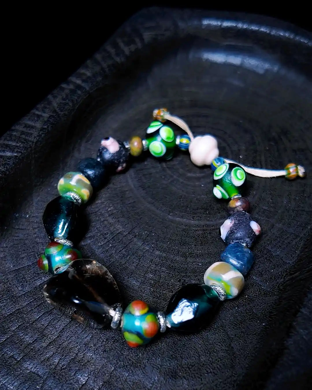 The Warden #32 smoky quartz and Tibetan dzi protection bracelet, full flat lay on dark wood showing complete bead arrangement with dzi fragment and evil eye glass