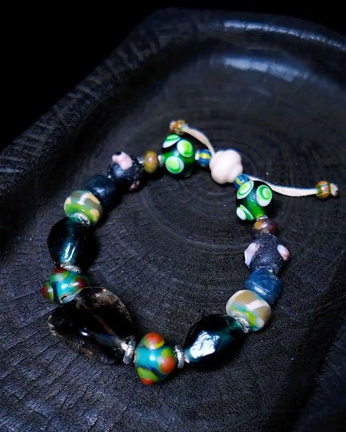 The Warden #32 smoky quartz and Tibetan dzi protection bracelet, full flat lay on dark wood showing complete bead arrangement with dzi fragment and evil eye glass