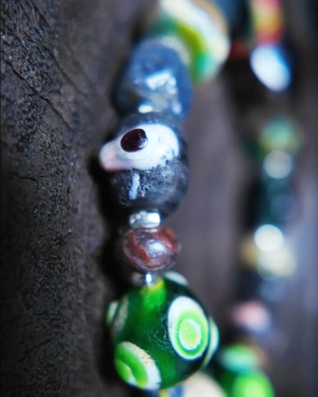 The Warden #32 smoky quartz and Tibetan dzi protection bracelet, detail view 4 — showing dragonfly eye, evil eye glass, raw sapphire, and red creek jasper accents