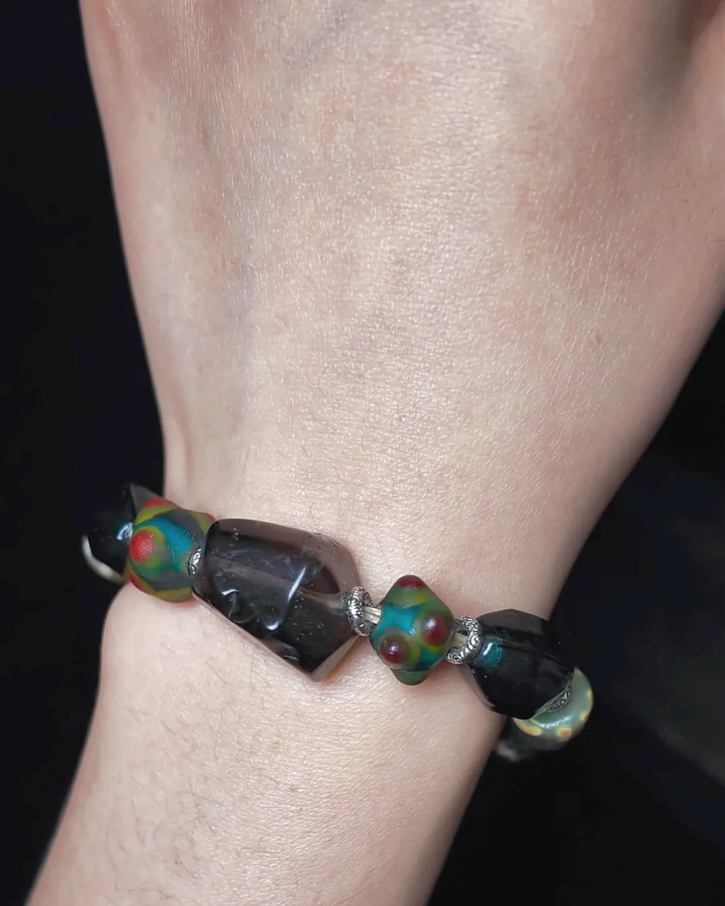The Warden #32 smoky quartz and Tibetan dzi protection bracelet, detail view 5 — showing dragonfly eye, evil eye glass, raw sapphire, and red creek jasper accents