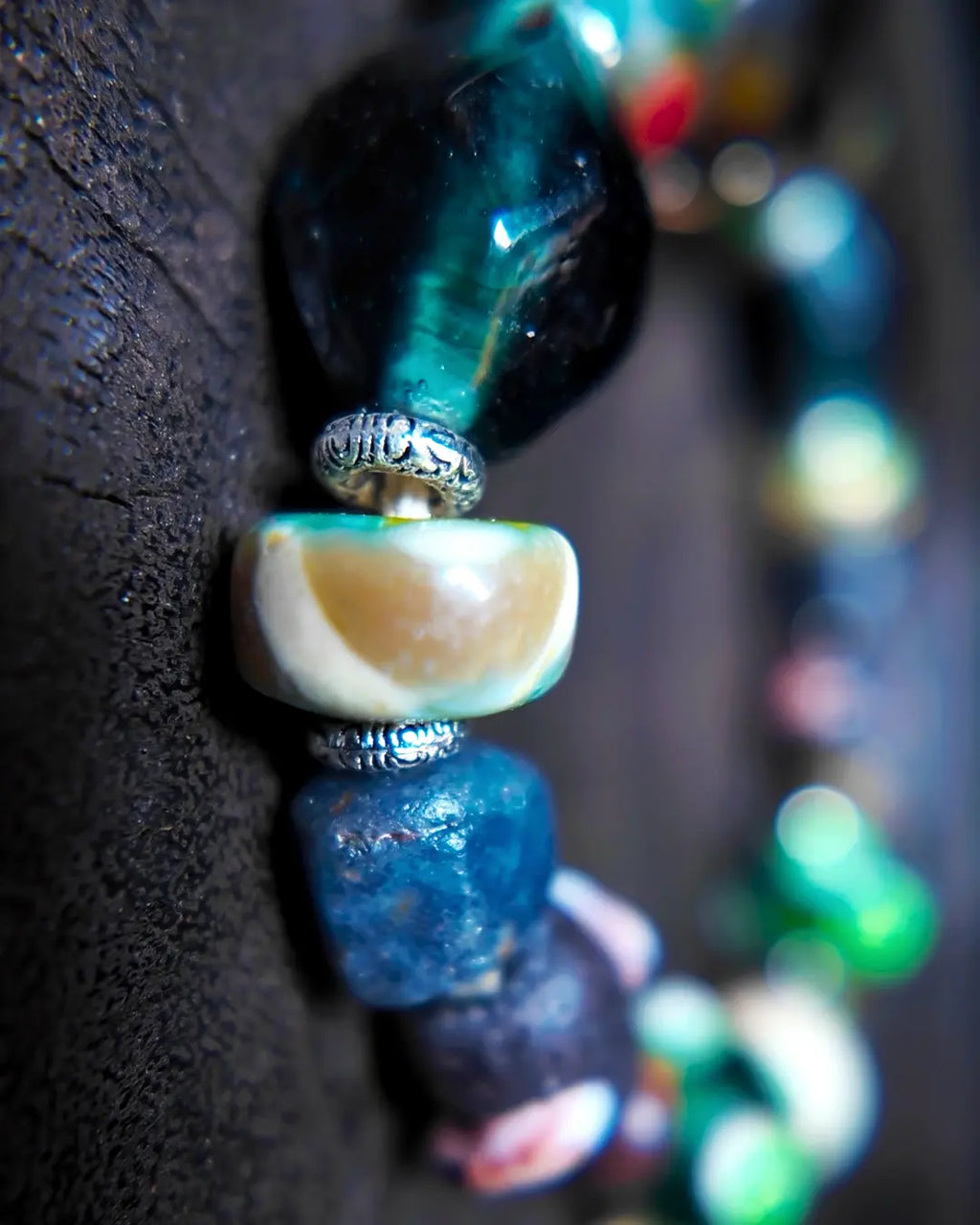 The Warden #32 smoky quartz and Tibetan dzi protection bracelet, detail view 6 — showing dragonfly eye, evil eye glass, raw sapphire, and red creek jasper accents