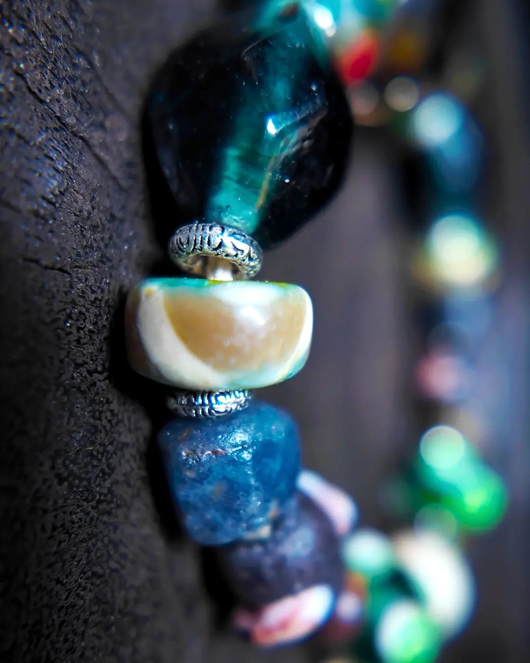 The Warden #32 smoky quartz and Tibetan dzi protection bracelet, detail view 6 — showing dragonfly eye, evil eye glass, raw sapphire, and red creek jasper accents