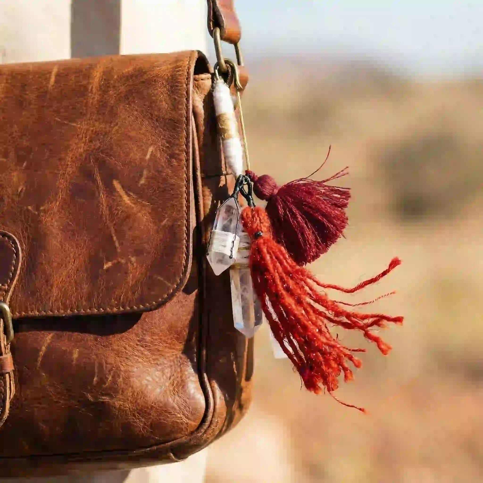 Brown leather bag with a bag charm with red tassels and Selenite stone
and clear quartz bead against a blurred natural background