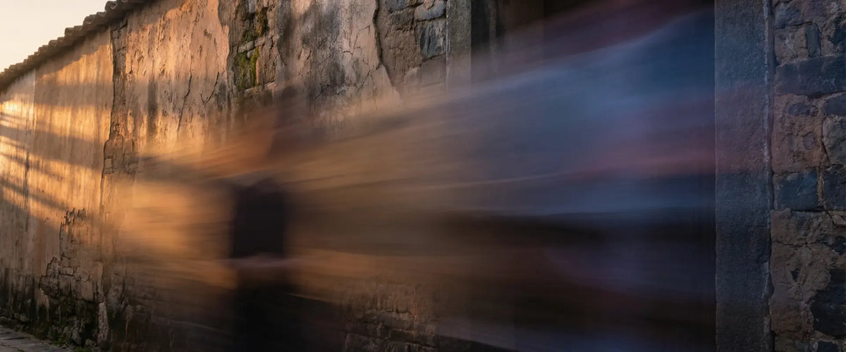 A long-exposure figure passing a stone wall, an editorial image about one-time movement