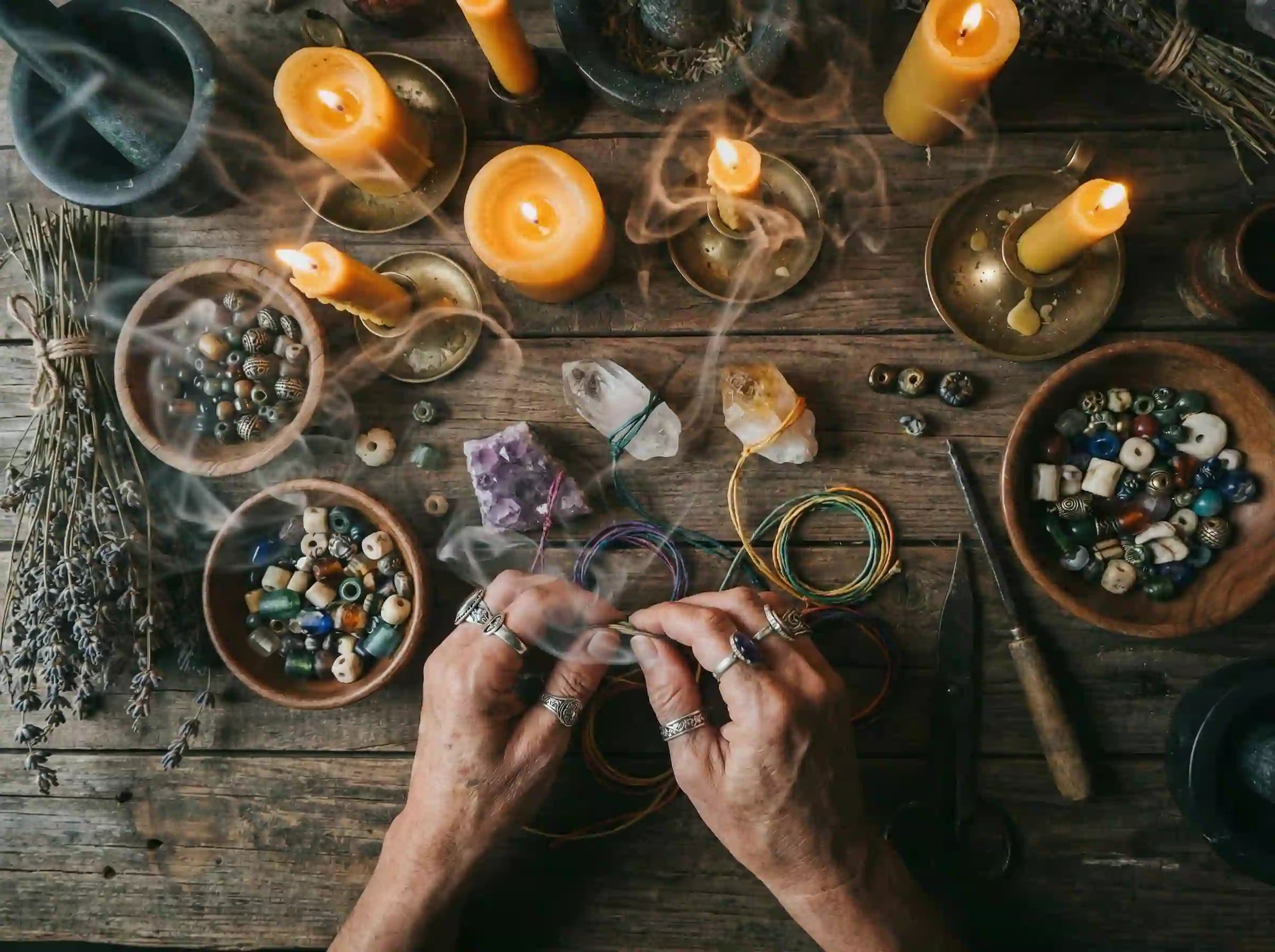 Hands working with himalayan quartz beads and candles on a wooden table.
