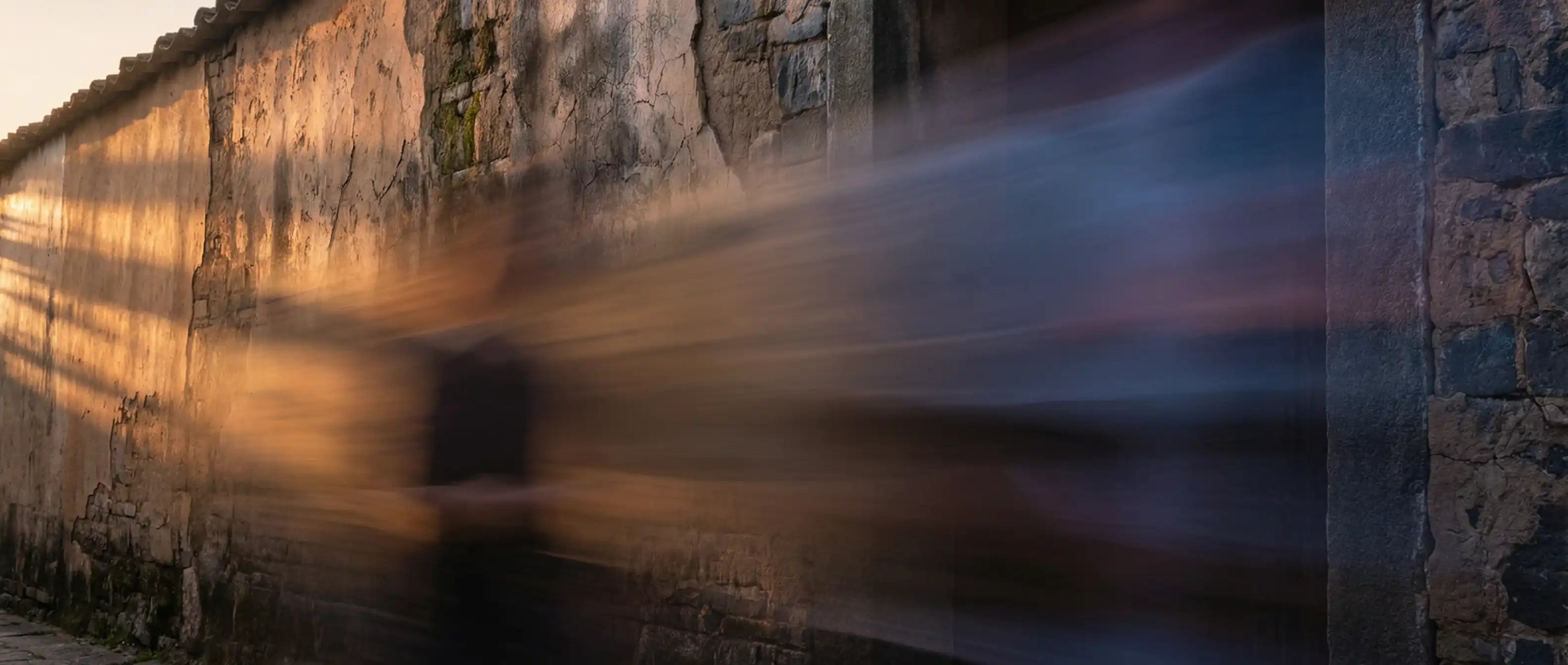 Long exposure of a person walking past a textured wall with warm light