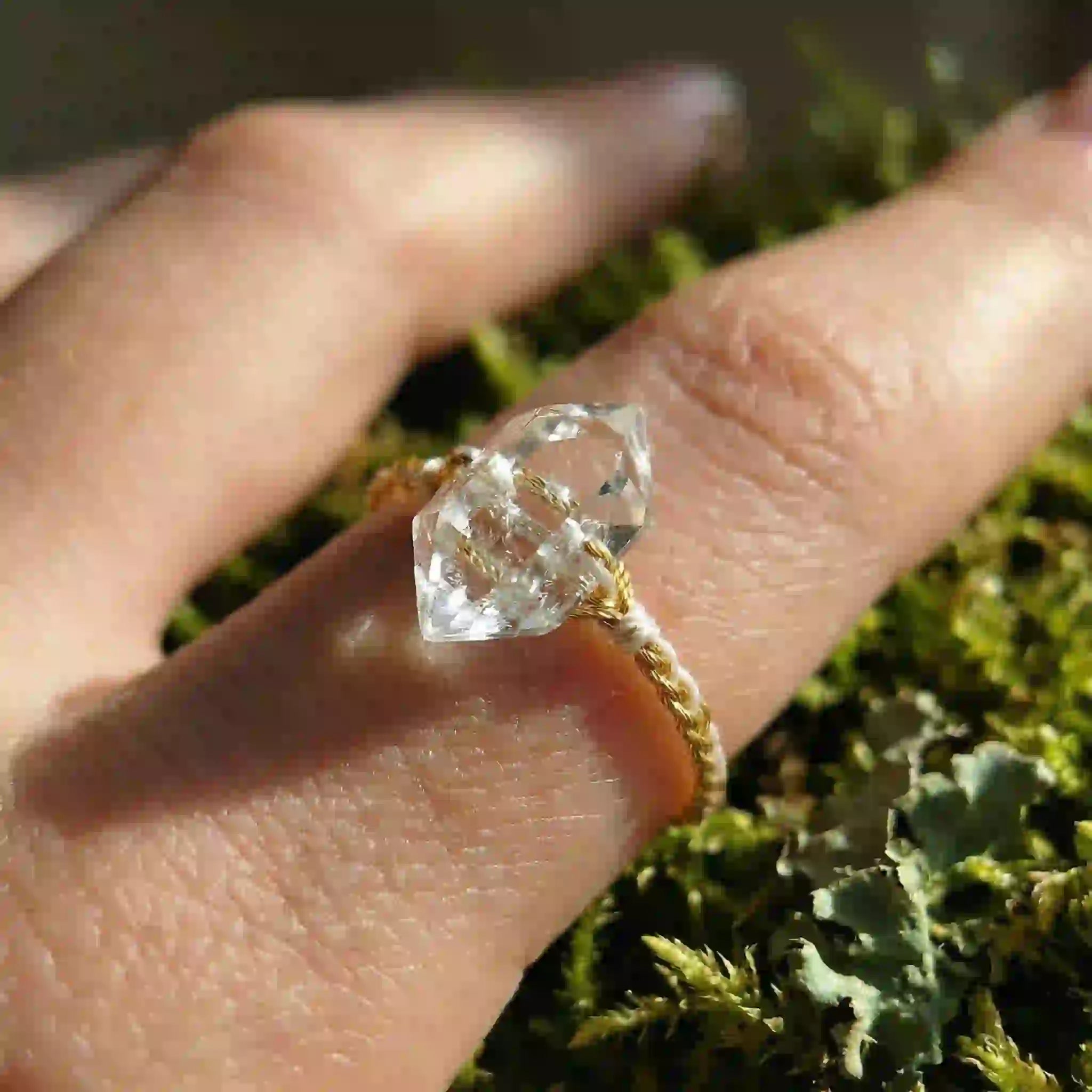 Hand wearing a braided ring with a clear crystal on a natural background