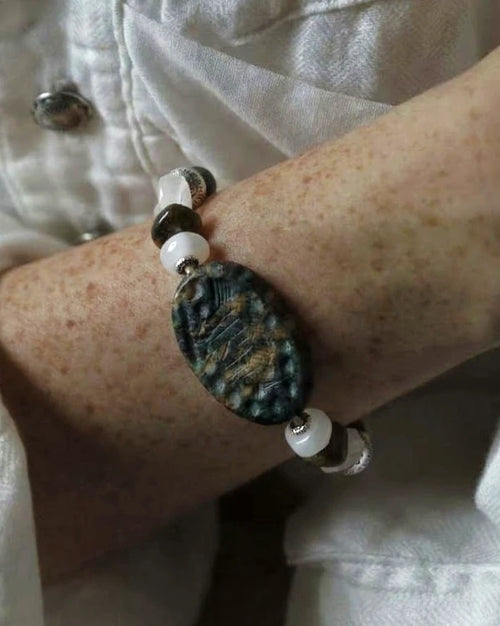 The Earthscript #57: Bracelet worn with a pale shirt, showing the carved green focal