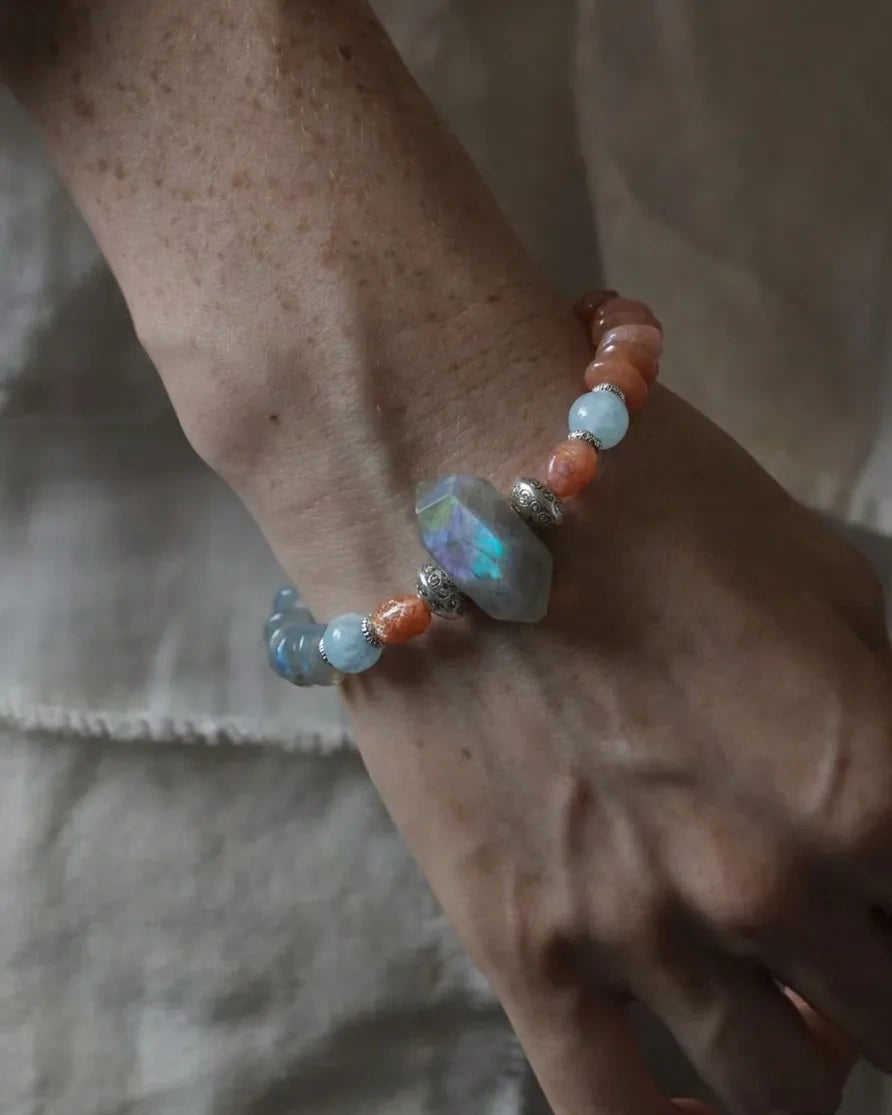 The Lucent #35 labradorite, sunstone and blue moonstone bracelet worn on a freckled wrist against linen