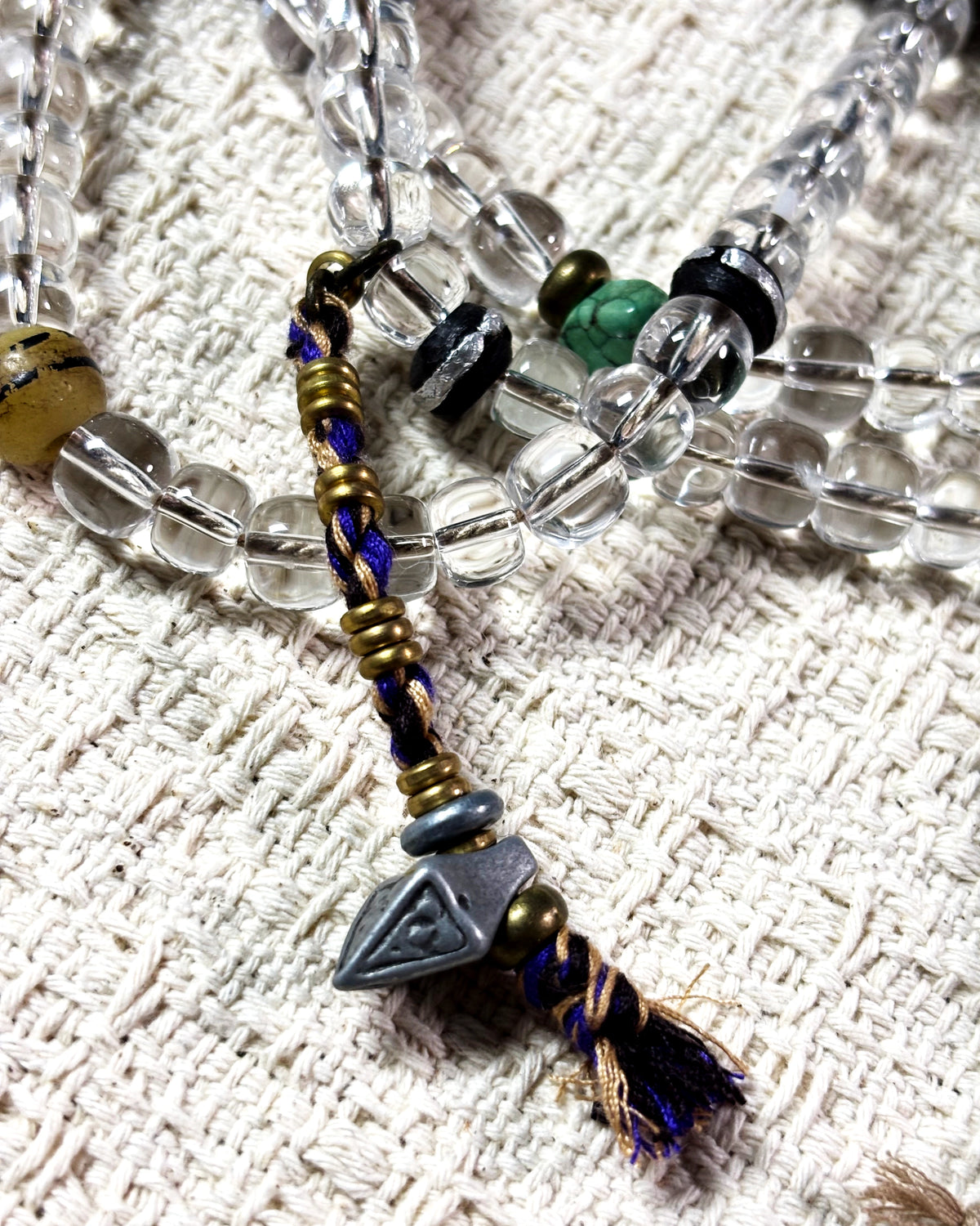 Brass counting beads and a Tibetan silver tsa-tsa marker threaded on a cotton mala counter