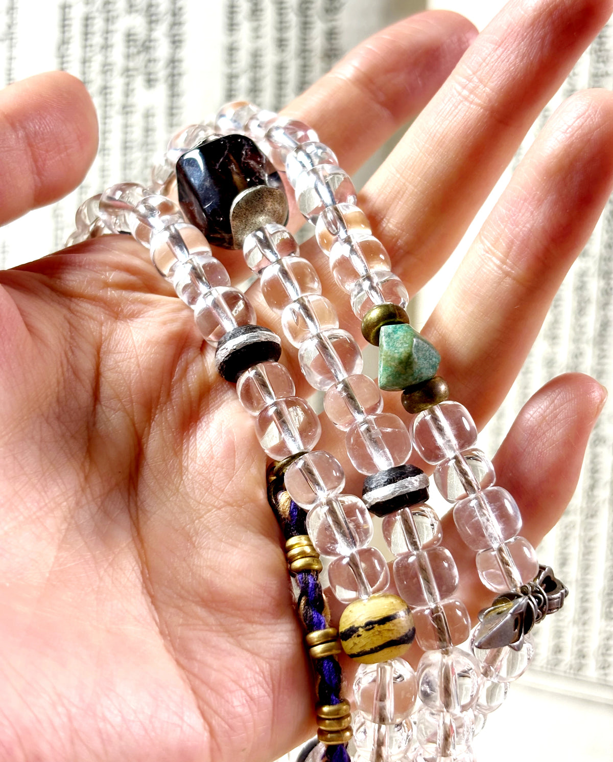 Clear quartz barrel beads, green turquoise accents, silver-inlaid ebony and yak-bone beads held in a hand