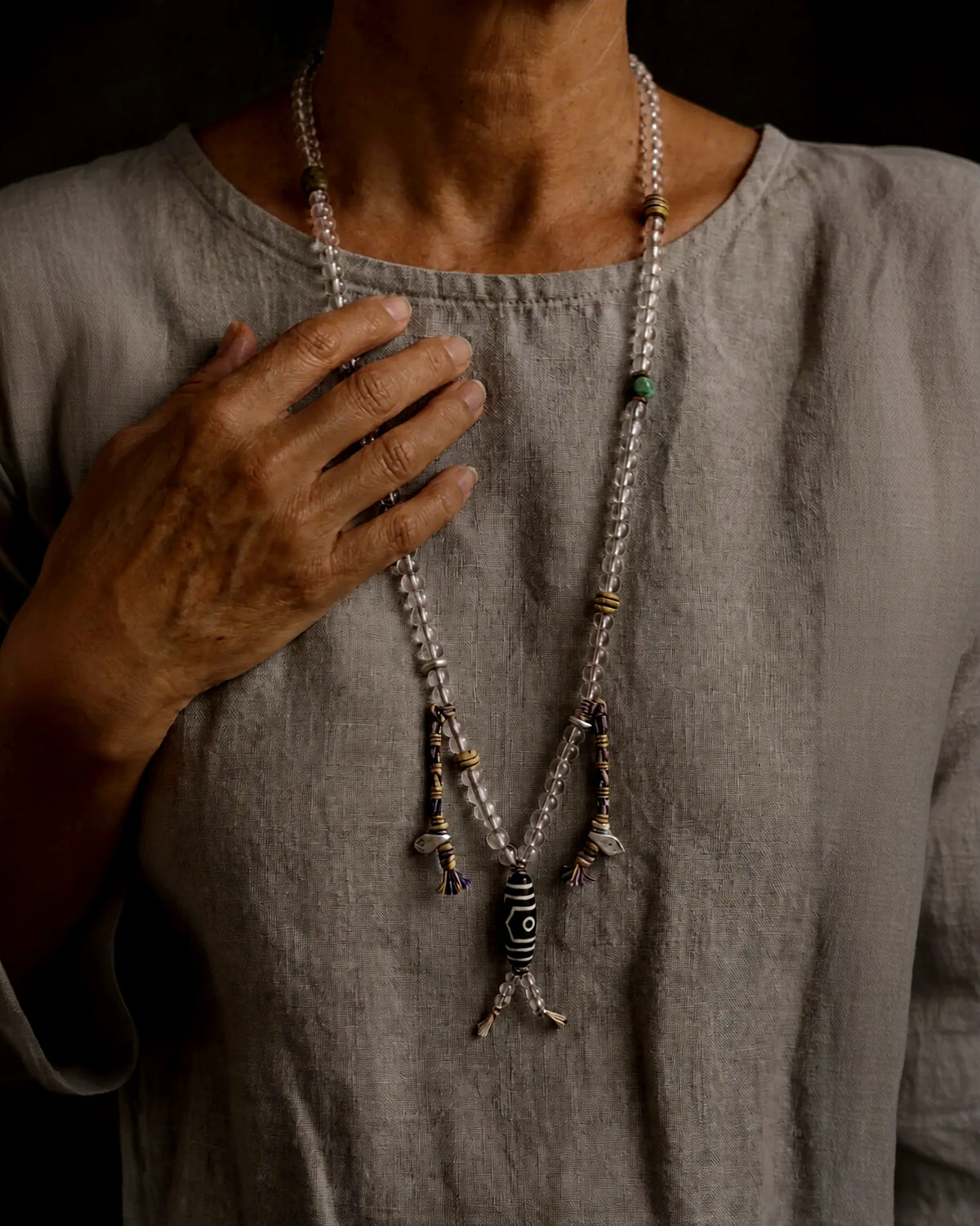 The Pilgrim #42 clear quartz mala worn as a long necklace, with a patterned agate guru bead and two counters
