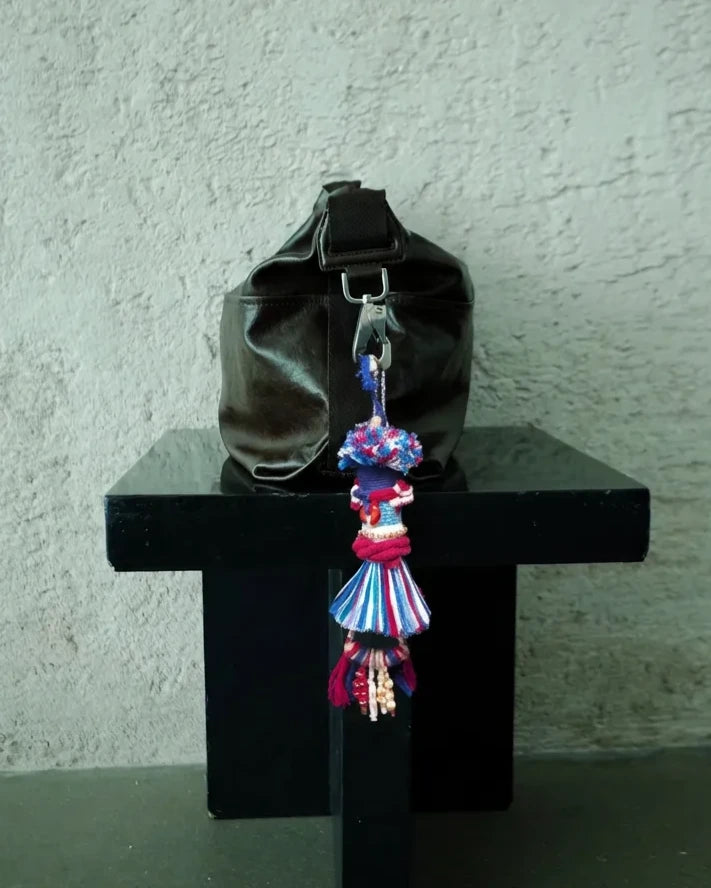 The Revel #43 cotton tassel bag talisman attached to a black leather bag for scale