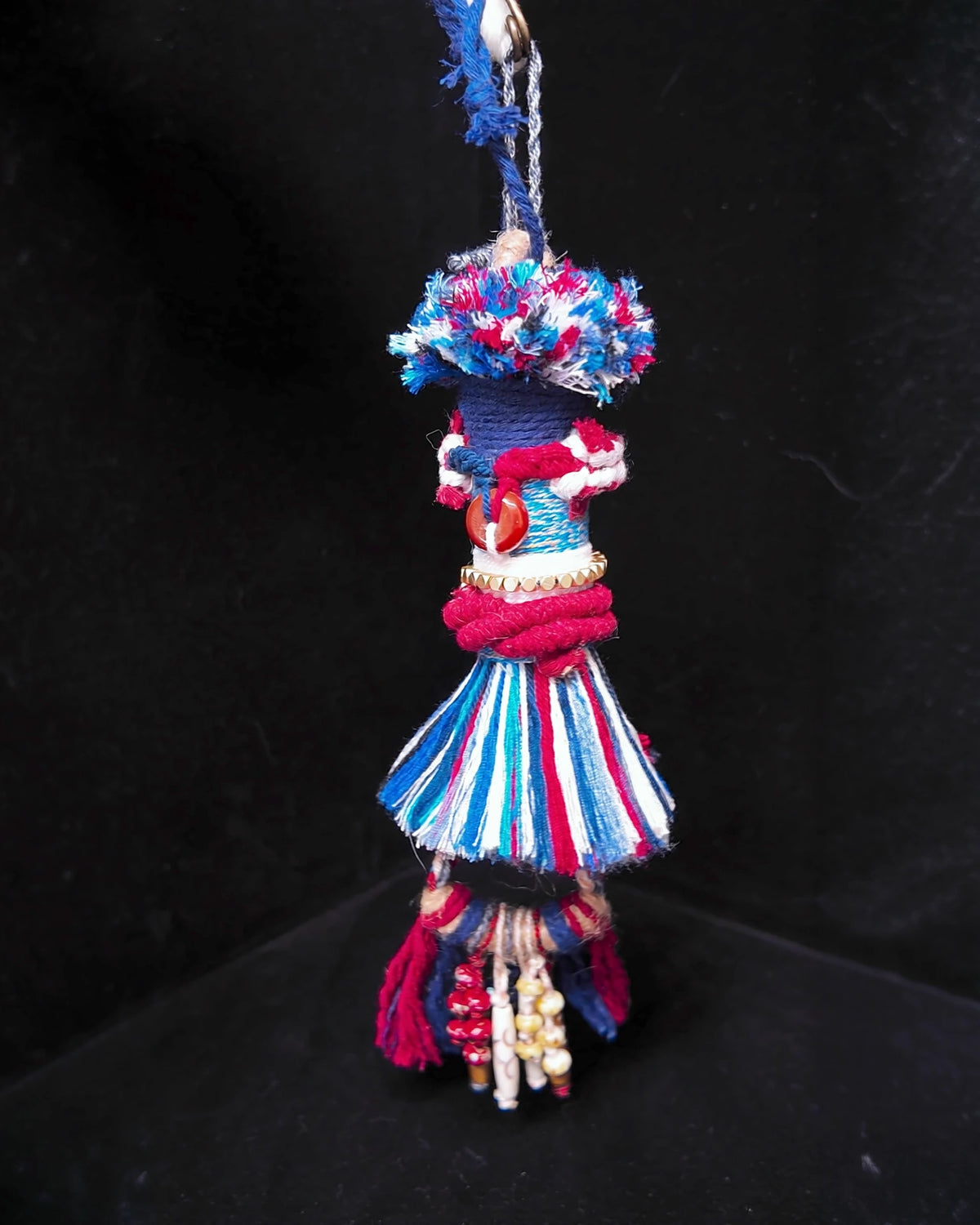 The Revel #43 hanging against a dark background with its cotton tassel and lower bead details