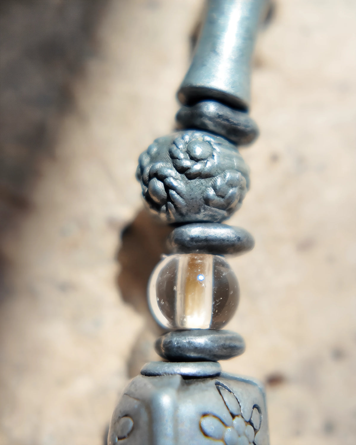 Textured decorative metal bead beside clear quartz and leather spacers